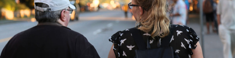 A community member walking beside a VocalEye volunteer sighted guide down the street.